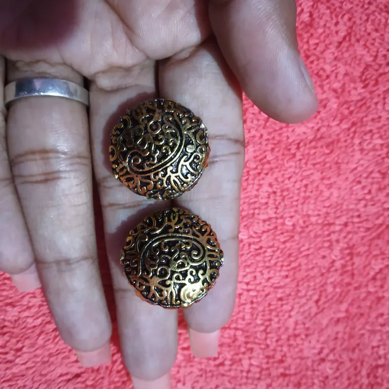 Original photo: two gold filigree earrings held in a palm over a pink towel